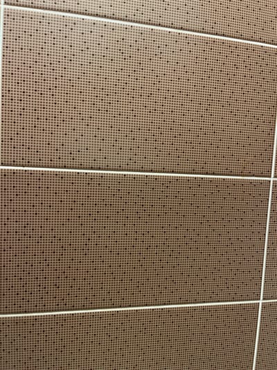 The image shows a close-up view of a tiled wall, likely in a bathroom or kitchen. The tiles are small and square, with a beige background and a pattern of darker brown dots arranged in a grid. There are horizontal grout lines that divide the wall into sections. No people or specific objects are visible, and no context is provided to determine the exact location within Quezon City, Philippines, other than it is an interior space. The lighting is even, suggesting artificial light.
