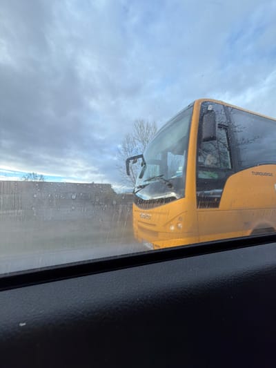 The image shows a yellow "Turquoise" bus seen through a vehicle window. The bus's front and side are visible, along with the number "69269". The sky is overcast. The window through which the bus is viewed has water droplets on it. The inside of the vehicle, specifically the dark interior trim, is visible on the right side of the frame. There is no indication of people or a specific location within Zlokuchene, Bulgaria.