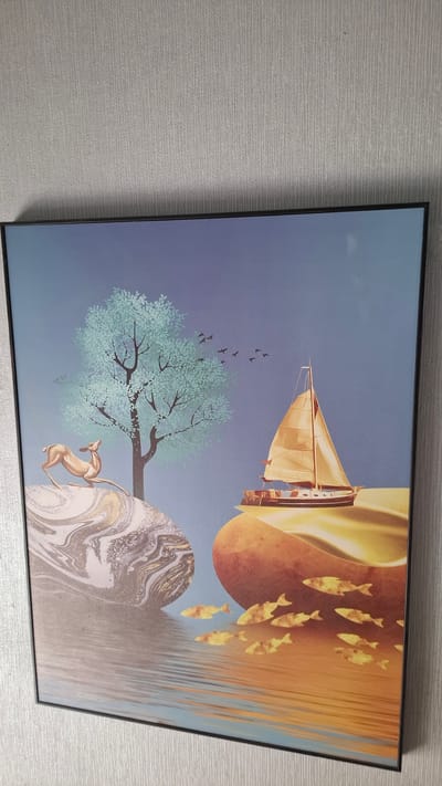 The image is a framed painting depicting a serene natural landscape with surreal elements. On the left, a golden deer stands on a marbled rock formation. A stylized tree with light green foliage rises behind the deer. In the background, a flock of small black birds flies across a blue sky. To the right, a sailboat with golden sails is positioned on a cliff-like structure that curves into the foreground. The water below the cliff reflects the warm colors of the sail and cliff, and a school of golden fish swims in the water. The painting has a dreamlike quality, combining realistic and stylized elements. The location in the city of Smolensk, Russia, is not depicted or suggested by the content of the image.