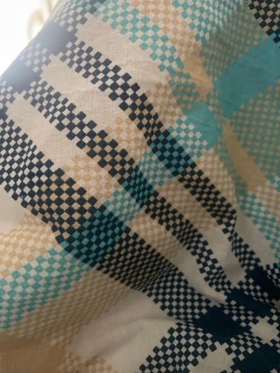 The image shows a close-up of a fabric with a checkered pattern. The colors in the pattern include white, beige, teal, and dark blue. The fabric appears to be draped or folded, creating soft shadows and highlights. There are no people, objects, actions, or interactions visible in the image. The location in the city of Ардонь, Russia is not determinable from the image.