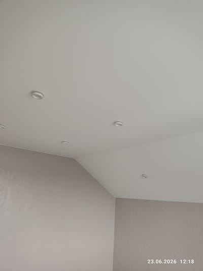 The image shows a ceiling with multiple circular light fixtures. The ceiling is painted a light gray color, and the walls are a slightly darker shade of gray. The light fixtures are evenly spaced across the ceiling, and they appear to be recessed into the ceiling. The image is taken from a low angle, looking up at the ceiling. There is a date and time stamp in the upper right corner of the image that reads "23.06.2026 12:18". There are no people or animals visible in the image. The overall impression is of a modern and clean interior space.