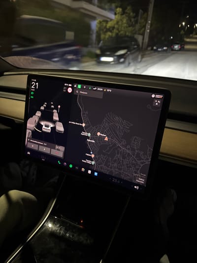 A screen displays navigation information within a vehicle. The map shows a route to Σαρωνίδα. The outside temperature is 12°C. The time is 20:24. The car's speed is 21 km/h. The battery level is 80%. The image indicates the presence of other vehicles in the vicinity, and the infotainment system shows a black interface. The current song is displayed as "Ρομαντισμός." The interior is dimly lit.