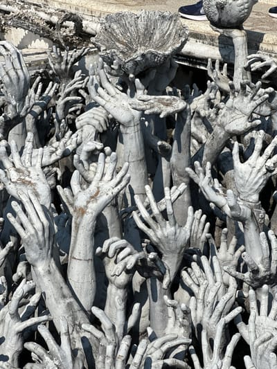 A densely packed arrangement of pale gray, sculpted hands and arms reaching upwards creates a haunting visual. The hands, depicted in various poses, convey a sense of desperation and reaching. Some arms emerge from a figure or structure with fragmented or distressed details. A sneaker is also visible in the upper left corner. The overall effect is evocative and symbolic, likely representing a struggle or plea.