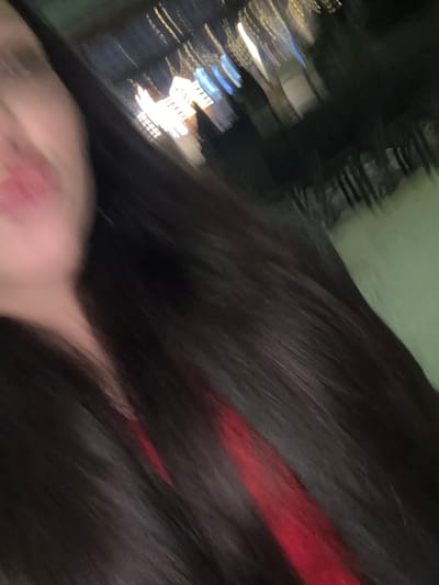 A blurry, angled shot captures a dark-haired person with a streak of red highlights. The background reveals blurred city lights at night, with indistinct buildings. The subject's face is partially visible, showing skin. The overall image has a shaky, out-of-focus quality, suggesting movement or quick capture. The angle and blur make the exact details unclear.