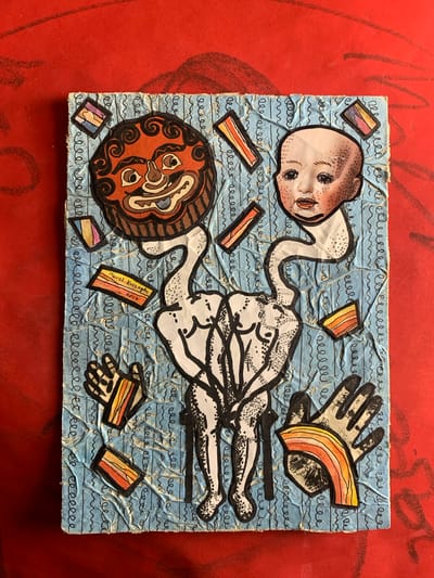 The image shows a piece of mixed-media art on a bright red, textured surface. The artwork itself is a collage on a light blue, crumpled background covered with black squiggly lines.

Dominating the center of the artwork is a stylized, anatomical torso rendered in black and white ink. The torso appears to be composed of two figures intertwined or fused together. Attached to the top of the torso are two distinct heads. On the left is a mask-like face with an exaggerated, grinning expression, featuring large eyes, a wide mouth, and curly black hair. On the right is a pale, disembodied baby's head with wide-set eyes, rosy cheeks, and freckles.

Scattered around the central figures are various small, colorful rectangular and diamond shapes with rainbow-like or striped patterns. To the left of the torso, there are two black and white drawings of hands. One hand is open with fingers spread, and the other is slightly curled. To the right of the torso, there is another drawing of an open hand, with a colorful, arched shape overlaying it.

A small orange rectangle in the lower left quadrant of the artwork contains handwritten text. It reads "Pavel Kuragin" and "2017".

The artwork is positioned on a flat surface with a prominent red texture, possibly a table or floor, with visible brush strokes or patterns. The lighting appears to be overhead, casting soft shadows.

The image is a photograph of the artwork and does not depict any specific location within Sergeevo, Russia, nor does it contain any information or context related to that city.