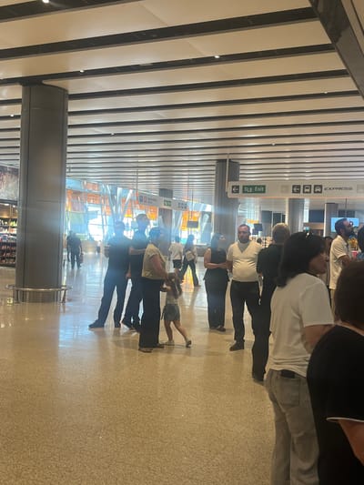 This media file captures a group of people in what appears to be a modern indoor public space, likely an airport or train station, given the signage and architecture. The scene is oriented vertically, suggesting the original capture was horizontal.
The subjects are a mix of adults and at least one child, some of whom are walking or standing in a line. Several individuals are wearing casual clothing like t-shirts and jeans. One person appears to be holding a child, who is positioned upside down. The overall mood seems neutral, with no strong indicators of emotion.
Notable details include a prominent sign with the word "EXPRESS" and an arrow, as well as another sign with the text "Tip Exit" and an arrow pointing left. These suggest transportation hubs or public access points. The flooring is a speckled, light-colored tile, and the ceiling features a modern design with parallel slats and lighting fixtures. The environment is well-lit, indicative of daytime. The location is identified as Parakar, Armenia.