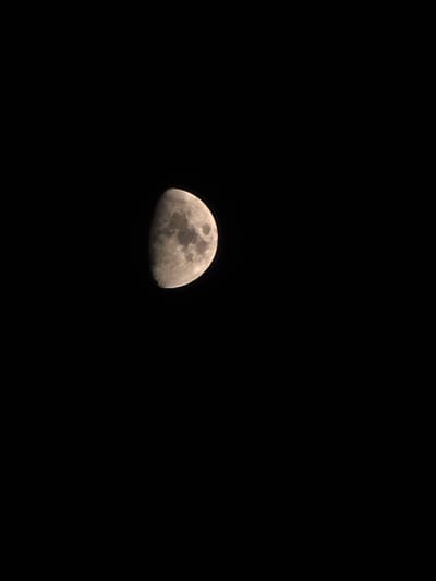 The image shows a close-up of the moon against a black, starless sky. The moon is approximately half-illuminated, with its surface exhibiting visible craters and lunar maria. The illuminated portion is on the right side of the moon and appears textured and greyish-brown in color. The rest of the moon is in shadow. The image is dark, with the black sky filling the majority of the frame, and the moon positioned in the upper left quadrant. There are no discernible landmarks, buildings, or other elements that would indicate a specific location, including the city of Montrouge, France. The scene is entirely focused on the celestial body.