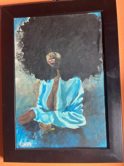A framed oil painting depicts a person with dark skin and a large black afro wearing a blue garment. The painting has a simple black frame. The subject is positioned off-center. The style is somewhat impressionistic with bold brushstrokes, especially visible in the rendering of the blue garment and the surrounding background. There's a signature in the bottom right corner that reads "Shades E".