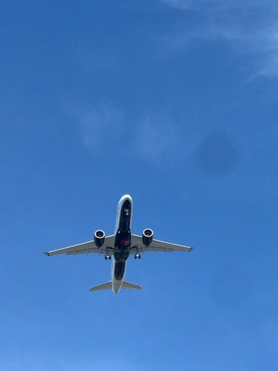 An underside view of a white passenger airplane is captured against a clear blue sky. The plane is in mid-flight, with its landing gear visible. The image appears to have been taken from a low angle, looking directly up at the aircraft. The location is the city of Richmond, Canada.