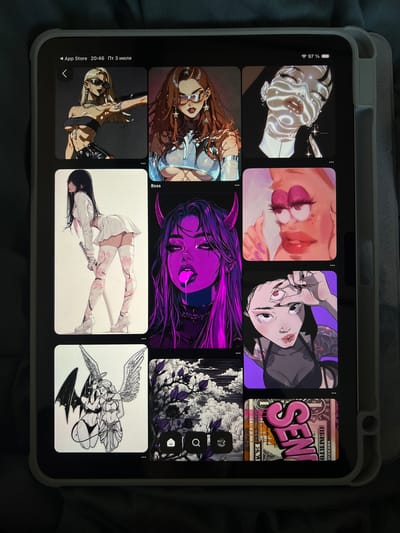 The image shows a tablet displaying a grid of artistic images. The tablet is resting on a dark gray fabric surface, possibly a blanket or bedspread. The tablet has a light gray protective case on its right side. The screen displays a Pinterest-like interface with various illustrations. From left to right, top row: a blonde woman with sunglasses, a woman with brown hair and sunglasses, and a close-up of a face with light patterns. Middle row: a woman in a white outfit holding a sword, a purple-hued illustration of a woman with devil horns, and a stylized depiction of Patrick Star from SpongeBob SquarePants. Bottom row: an illustration of two winged figures, one with dark wings and the other with light wings, a black and white illustration of trees and clouds with purple accents, and a close-up of a US dollar bill with pink text that reads "SEN". There is no information in the image to suggest the location is Genemuiden, Netherlands.