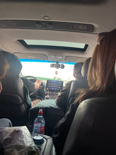 A view from inside a car in Stalskoye, Russia. One person is driving while a passenger occupies the front seat. A touch screen infotainment system is visible in the dashboard. A water bottle is next to the front passenger.