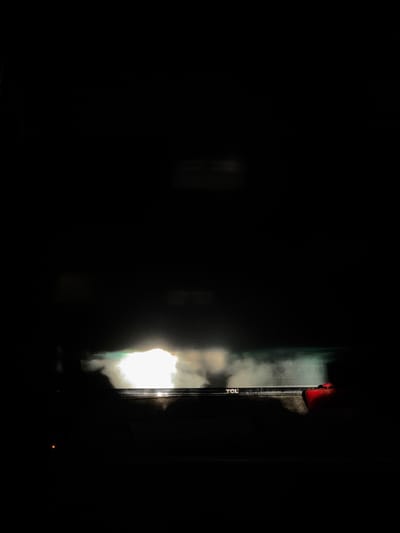 The image shows a dimly lit indoor scene at night. A TCL television is visible on the right side of the frame, with its screen emitting a bright light that creates a shadow. At the top of the screen, a red object is partially visible. The setting appears to be a room within a building. The presence of the TCL television and the absence of specific contextual cues do not allow for the determination of a precise location in Boulder, United States.