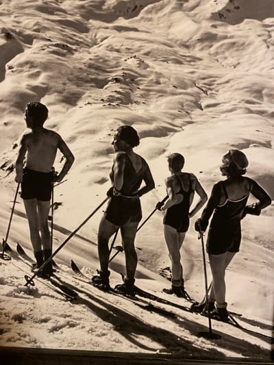 This is a black and white photograph, oriented vertically, depicting a group of four skiers descending a snowy slope. The skiers are positioned one behind the other, suggesting a race or a training exercise. They are all wearing athletic attire suitable for skiing, including shorts and what appear to be goggles on the top-most skier. Their skis and poles are clearly visible, planted in the snow or in motion.
The scene is dominated by the texture of the snow, which is uneven and appears to be a natural, ungroomed slope. The lighting suggests it could be daytime, with shadows cast by the skiers, though the exact time of day is difficult to determine from the monochromatic image. There are no clear indications of specific weather conditions beyond the presence of snow.
The location context is given as Ленинское, Russia, which implies a setting in that region. The individuals are focused on their activity, with their body language indicating exertion and concentration. There is no visible text within the image itself. The overall impression is one of a dynamic sporting event or practice session in a rugged, snow-covered environment.