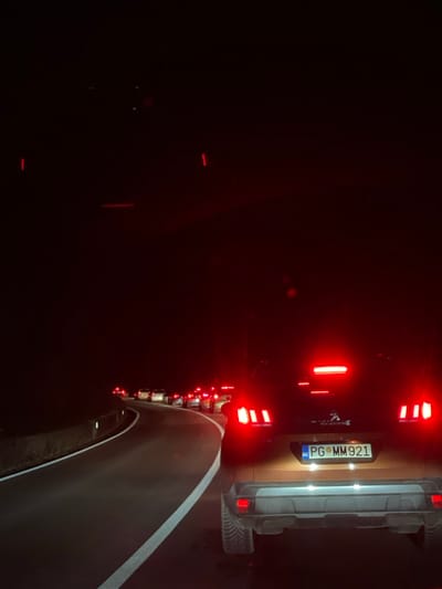 A nighttime traffic jam with rows of red tail lights illuminating the darkness. The closest vehicle, a tan-colored SUV, displays a license plate "PG MM921". A partial view of the highway lane markings are visible. The road seems congested.