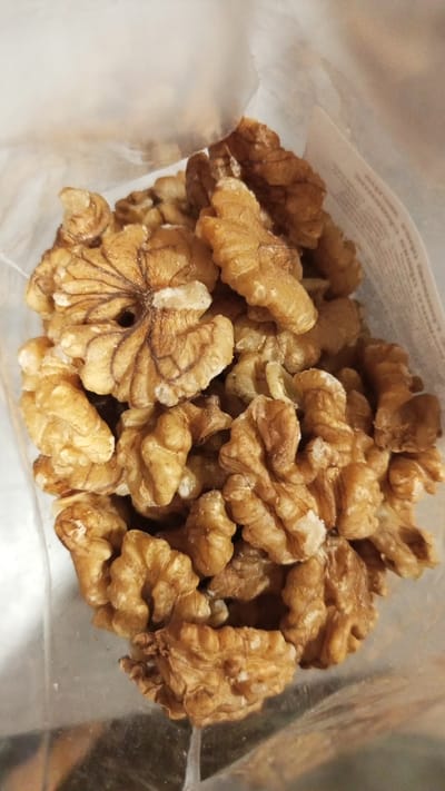 The image shows a close-up view of a pile of shelled walnuts inside a clear plastic bag. The walnuts are mostly halves, with a light brown color and visible ridges. The bag is partially transparent, allowing a glimpse of the surrounding environment, although details are limited. The image was taken in Юдино, Russia.