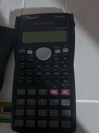 A black Kenko KK-82MS calculator is lying on a white surface. The calculator has a display screen and several buttons. It is a scientific calculator. The image provides no information about the location in San Juan de Los Morros, Venezuela, or any people, actions, or interactions.