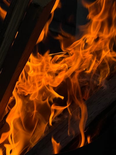 This media file is a close-up shot of a fire. The subjects are flames and pieces of wood, suggesting a bonfire or a fireplace. The scene is dark, with the bright orange and yellow flames being the primary light source. The wood appears dry and is positioned at an angle, with some pieces layered over others. Wisps and tendrils of fire are captured in motion, creating a dynamic and fluid appearance against the dark background and the solid forms of the wood. There are some small, glowing embers visible, particularly between the pieces of wood.
The activity taking place is combustion, with the wood burning and producing flames and heat. The time of day is implied to be dark, likely nighttime or a very dimly lit environment, due to the prominence of the fire's glow and the deep shadows. There are no people visible, and no explicit weather cues are present, although the setting suggests an outdoor or a well-ventilated indoor location suitable for a fire. The overall mood conveyed is one of warmth, energy, and perhaps a touch of intensity due to the vibrant flames. No text is visible in the image. The location context provided is Solontsy, Russia.