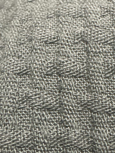 The image shows a close-up, macro view of a textured, grey fabric. The fabric appears to be woven with a consistent pattern of intersecting threads, creating a grid-like structure with raised areas. The lighting suggests the texture is being illuminated from the side, casting subtle shadows that highlight the three-dimensional nature of the weave. There are no people, objects, or environmental features visible that would allow for identification of a specific location within Letterkenny, Ireland. The scene is purely textural.