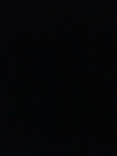 The image is predominantly black, suggesting a nighttime scene or a very dark environment. Several faint white specks are scattered across the darkness, resembling stars in the night sky or possibly dust particles on a dark surface. The overall composition is simple and stark, emphasizing the contrast between the void and the tiny points of light.