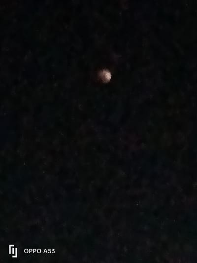 This image displays a single, luminous, roughly spherical object against a dark, featureless background, consistent with a night sky. The object, which appears to be a celestial body such as the Moon, is positioned in the upper-central portion of the frame and exhibits a pale, slightly blurred, off-white to pale orange hue. No other distinct celestial bodies, terrestrial features, individuals, or man-made structures are visible. A "OPPO A53" watermark is present in the lower-left corner. The scene is located in Riabai ward, Kenya.