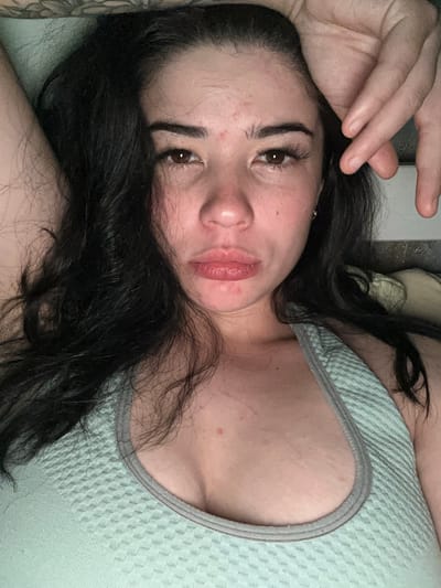 The image shows a close-up, overhead shot of a woman lying down. She has dark hair and is wearing a light blue tank top. Her left arm is raised above her head, and her right hand is resting on her forehead. The woman's face is visible, and she appears to be looking directly at the camera with a neutral expression. The background is out of focus, but suggests an indoor setting. There is no information provided in the image or accompanying text that would allow for the identification of a specific location in Gavrilov Posad, Russia.