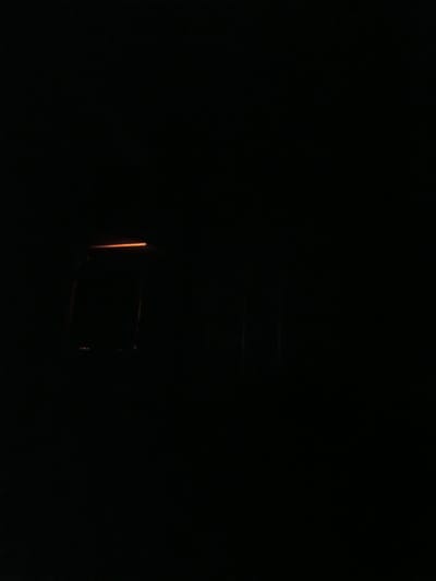 The image depicts a dark interior scene. In the center, a faintly illuminated, rectangular object is visible, resembling a window or a screen, with an orange glow emanating from its top edge. The rest of the image is predominantly black, with some indistinct vertical lines or shapes appearing on the right side. No people or specific environmental details are discernible beyond the object and the overall darkness. The location of Mikhnevo, Russia, cannot be determined from the visual information provided.
