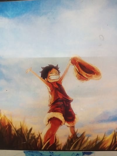 The image is a painting of a young boy with dark, spiky hair and a wide, joyful smile, wearing a red sleeveless shirt and shorts with a furry trim. He is standing in a field of tall, golden grass under a bright, cloudy blue sky. The boy is holding up a straw hat with his right hand, which is extended above his head. His left arm is also raised in a gesture of excitement. The style of the painting is reminiscent of anime or manga. There is no visible indication of the city of Turumame, Indonesia, or any specific urban setting within the image itself. The scene is outdoors in a natural, grassy environment.
