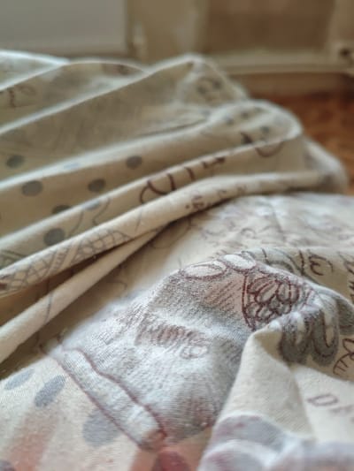The image is a close-up, shallow depth of field shot of a beige fabric with a subtle pattern of gray dots and brown floral designs. The fabric is creased and folded, creating a sense of texture and dimension. The lighting suggests it is indoors, possibly in a home environment. There is no indication of a specific location within Etulia, Moldova, as the scene is abstract and lacks any identifying landmarks or context. The image focuses solely on the textile.