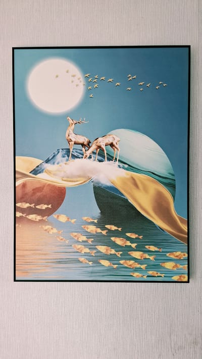 This is a photograph of a framed piece of art hanging on a textured white wall. The artwork depicts an abstract landscape with surreal elements. In the upper left quadrant, a large, luminous white circle, possibly representing a moon or sun, is partially obscured by a flock of small yellow birds flying towards the right. Below this, two deer are standing on a cloud-like formation on top of abstract mountainous shapes rendered in blues and whites. Flowing elements in warm oranges and yellows create a sense of movement and depth across the mid-section of the artwork. The lower portion of the image features a body of water with numerous golden-hued fish swimming in schools, depicted with a textured, almost metallic sheen. The overall color palette is a blend of cool blues and warm earth tones. The photograph is taken from a slightly downward angle. The location of the artwork within the city of Smolensk, Russia, is not determinable from the visual information provided in the image.