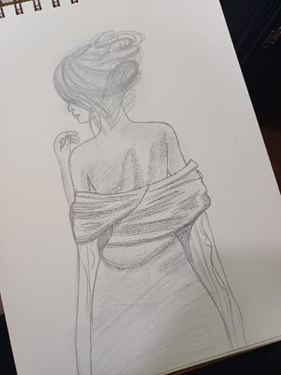 The image displays a monochrome pencil sketch of a female figure on a sheet of white paper, which is part of a spiral-bound sketchbook. The sketch depicts the figure from the back, turning her head to her left to look over her shoulder. Her hair is styled in an elaborate updo with multiple buns. A garment, possibly a shawl or wrap, is draped around her shoulders and back, leaving her upper left shoulder and back exposed. Her left hand is raised towards her face, with fingers slightly curled. The drawing exhibits visible pencil strokes for outlining and shading. The scene is located in 서대문구, South Korea.