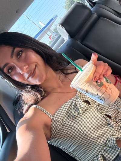 The image shows a woman in a car holding a Starbucks drink. She is wearing a green and white checkered top. The car's interior is black leather. Through the car window, a gas station sign is visible, which may be located in Santa Ana Xalmimilulco, Mexico.