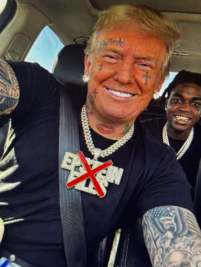 The image shows a man with tattoos on his face, neck, and arms, wearing a black t-shirt and a large jeweled pendant. He is in a car, with another person visible in the background. The man in the foreground has blonde hair and appears to be imitating a public figure. The environment is inside a vehicle, likely a car, with a view of the sky through the window. There is no indication of the location being in Shcherbanka, Ukraine.