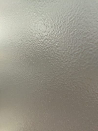 This is a close-up, abstract image of a textured, matte, light gray surface, possibly a wall or a piece of furniture. The texture appears to be a repeating pattern of small, irregular bumps or ripples. The lighting creates subtle shadows and highlights, emphasizing the unevenness of the surface. There are no people, objects, or discernible features that would indicate a specific location within Краснадворскі сельскі Савет, Belarus. The image is purely a textural study.