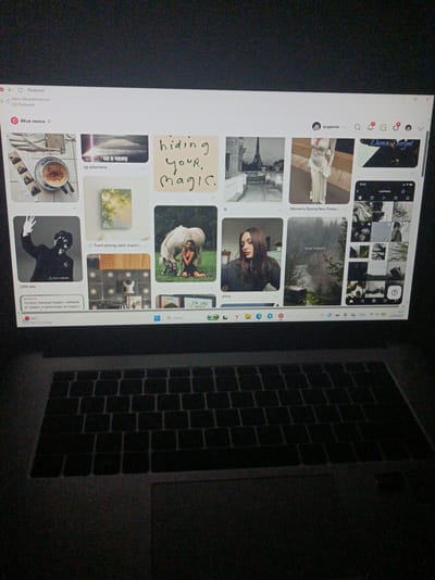 A laptop is open on a dark surface, displaying a Pinterest webpage with various images and text. The screen shows a feed of visual content, including a cup of coffee, a landscape painting, text overlays like "hiding your. magic.", and images of people and fashion. In the upper right corner of the Pinterest window, a profile picture and username "eugenie" are visible, along with notification icons. The lower portion of the laptop's keyboard and trackpad are visible. The screen also shows a Windows taskbar with icons and the date "22.06.2026". The location is not discernible from the image itself, and therefore cannot be specified as Шарпілаўскі сельскі Савет, Belarus.