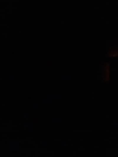 The image is extremely dark, with very little visible detail. In the upper right quadrant, there is a faint glow of reddish-orange light, suggesting a distant light source or reflection. The rest of the image is predominantly black, making it impossible to discern any specific objects, people, or environmental features. There is no discernible context related to the city of Orzhiv, Ukraine.