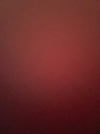 This media file is a photograph with a grainy texture, primarily displaying a solid, dark red or burgundy color. The lighting appears to be uneven, with a gradient that shifts from a lighter, more reddish hue on the left side to a deeper, almost blackish red on the right side, suggesting a light source positioned to the left and possibly slightly in front of the subject.

There are no discernible subjects like people, objects, or a specific scene. The image appears to be a close-up or abstract view of a textured surface. The texture itself is consistent throughout, appearing as small, irregular speckles or grains across the entire frame.

No activity or event is taking place, as there are no figures or elements that suggest action. There are no location cues, time of day indicators, or weather-related details. The overall impression is one of a uniform, textured background. No text is visible in the image. The context of Malete, Nigeria, does not provide any specific visual clues within the photograph itself.