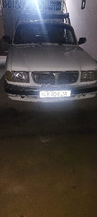 A white pickup truck is parked on a dark surface. The truck faces the camera with its headlights and front grill visible. A license plate is mounted on the front, displaying "10K 859 JA". The truck's side mirrors and cabin are partially visible. The surrounding area is dark, suggesting an indoor or nighttime setting. The image is slightly rotated, causing the truck to appear tilted.