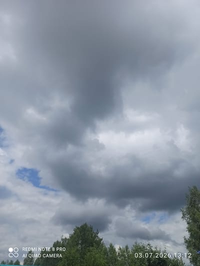The image shows a cloudy sky over a treeline. The sky is filled with dark gray clouds, with some patches of blue sky visible. The treeline consists of green deciduous trees. In the bottom left corner, there is a watermark that reads "REDMI NOTE 8 PRO AI QUAD CAMERA." In the bottom right corner, a timestamp is visible: "03.07.2026 13:12." The image was likely taken in Sovetskiy, Russia, given the timestamp format which includes a year in the future, suggesting a potential placeholder or an error in the metadata.