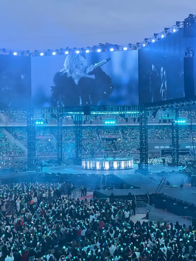 The image captures a concert scene, likely taking place at night in what appears to be an outdoor stadium. A large screen displays a performer, possibly a singer, whose image is visible. The stadium is filled with a crowd of people, many of whom are holding up lights, creating a sea of illumination. Stage lighting and other stadium fixtures are also visible.

Given the location in Goyang-si, South Korea, it's plausible the concert is taking place at one of the city's larger venues such as the Goyang Stadium or a similar large-scale arena.