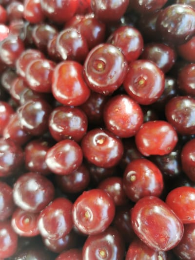 The image displays a close-up, overhead view of a large pile of ripe cherries. The cherries are a deep red color and appear to be fresh, with some water droplets visible on their surfaces. They are tightly packed together, creating a textured mosaic of rounded shapes. The lighting creates highlights and shadows on the fruit, emphasizing their glossy appearance. There are no people or other objects visible in the frame. The scene is a natural, food-related subject. The location in Pociumbeni, Moldova, suggests this is likely a depiction of locally grown produce or a market display.