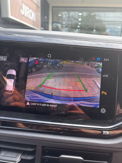 The image shows a rearview camera display in a car, likely a backup camera. The display shows a rear view of a parking space with a red line indicating the projected path of the vehicle as it backs up. Green lines indicate the limits of the projected path.  The car is in reverse, indicated by the "P" icon.  The display also shows a warning that reads "Look! Is it safe to move?".  A digital clock at the top right corner of the display indicates that the time is 2:21. The image was taken in San Rafael, Costa Rica, based on coordinates 9.938, -84.153.