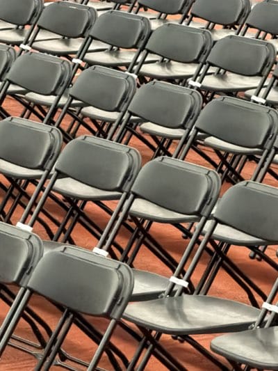The image shows rows of black folding chairs on a reddish-brown floor. The setting appears to be indoors, possibly in a large room or auditorium in Rochester, United States. The chairs are uniform in design, and the composition suggests a large number of seats are prepared for an event. No people are visible in the frame.