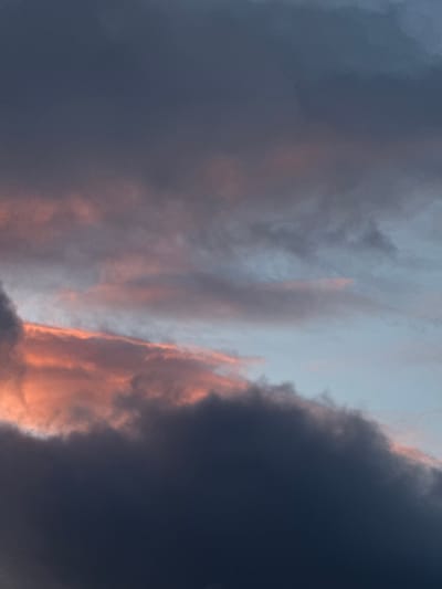 The media file presents a dramatic and atmospheric sky scene, dominated by a dynamic interplay of clouds at what appears to be either sunrise or sunset. The sky is filled with expansive cloud formations, exhibiting a striking range of colors.
Large, dark grey and deep blue clouds occupy significant portions of the frame, suggesting heavy cloud cover or an impending weather event. These darker masses are contrasted vividly by streaks and patches of brilliant orange and soft pink, which illuminate the edges and undersides of some clouds. These warm hues indicate that the sun, though not directly visible, is low on the horizon, casting its light onto the cloud formations. Lighter, more ethereal blue-grey sections of the sky are also visible between the darker cloud masses.
There are no people, man-made objects, or specific activities depicted in the image. The scene is purely a natural landscape of the sky, focusing on the atmospheric conditions and the captivating effect of light on clouds. No visible text is present. The general impression conveyed is one of awe-inspiring natural beauty and dramatic weather dynamics, consistent with a spectacular start or end to the day over Fécamp, France.