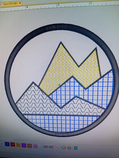 The image displays a digital rendering of an embroidered design, likely within an embroidery software program. The design is circular and features stylized mountain peaks. The peaks are filled with different patterns: the highest peaks are filled with yellow dots, the middle layer with blue cross-hatching, and the lowest layer with gray zig-zag lines. The entire design is enclosed within a thick, dark circular border. The background of the image is a light gray, and a ruler with numerical markings is visible at the top, suggesting a digital interface. A toolbar with various icons and numbered buttons (9, 10, 11, 12, 13, 14, 15) is present at the bottom of the screen, further confirming it's a computer-generated image within a design program. There are no people, interactions, or environmental details present that would allow for placement in Rumuepirikom, Nigeria or any other geographical location.