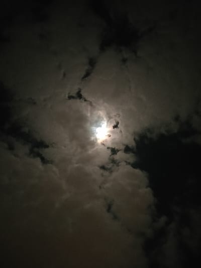 A night scene reveals a glowing orb, likely the moon or sun, obscured by layers of dark, ominous clouds. The clouds vary in density, with some appearing thick and dark, while others are lighter and more translucent, allowing light to filter through. The darkness surrounding the light source creates a dramatic and slightly unsettling atmosphere. The image has an overall dark and mysterious tone.