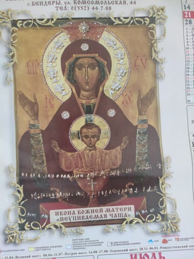 The image is a close-up of an Orthodox icon of the Mother of God, specifically the "Unfading Cup" icon, set within an ornate golden frame. The icon depicts the Virgin Mary holding the Christ child. The title of the icon is written in Russian below it.

The background of the image contains text that appears to be from a calendar, with dates and other information, also in Russian. To the right of the icon, there is a column of dates. To the left and below the icon, there are descriptions related to fasting periods. One line of text near the bottom edge of the image mentions "08.06-11.07 – Peter's Fast; 14.08-27.08 – Dormition Fast; 28.11-06.01 – Nativity Fast."

The text at the top of the image appears to be a location and contact information. It reads "g. BENDERI, ul. Komsomolskaya, 44 TEL: 0(552) 44-7-88". Bender (or Tighina) is a city in Moldova. Blizhnii Khutor is a village within the administrative jurisdiction of the city of Tighina. Therefore, the location mentioned in the text, Bender, is relevant to Blizhnii Khutor, Moldova, as it refers to a nearby administrative center.

The image is a photograph, likely taken in daylight given the lighting. The focus is primarily on the icon and its frame. The other elements, the calendar and descriptive text, are secondary and serve as context.
