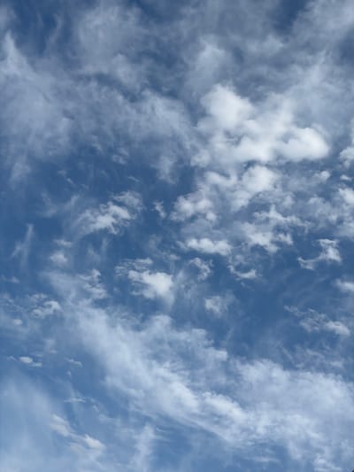 This is a full-frame, eye-level shot looking straight up into a partly cloudy sky on a bright, overcast day. The clouds are white and wispy, appearing to be cirrus or altocumulus formations. They are spread across a deep blue sky, with varying degrees of density. Some areas are more opaque with bright white clouds, while others are thin and translucent, allowing the blue sky to show through. The light suggests it is daytime, possibly late morning or early afternoon, given the brightness of the clouds. There are no discernible objects or people in the frame, and no text is visible. The scene is a natural outdoor setting. The location context of Dachi Su, Kyrgyzstan, does not provide specific visual cues within the image itself, but it indicates a general geographic setting. The overall impression is one of a calm, expansive sky.