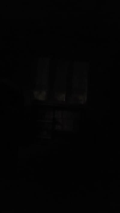 The image depicts a dark, dimly lit interior that appears to be a room with windows. Faint light filters through what seem to be window panes, revealing subtle shapes and outlines of objects within the space. The overall impression is one of low visibility and a somber atmosphere. The image does not contain any identifiable landmarks or features that would allow for pinpointing a specific location within Yandare, Russia.