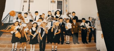 The image is a photograph of a group of children and a few adults on a set of stairs outside a building. The children appear to be dressed for a school event, many holding bouquets of flowers and some wearing medals. The setting appears to be a formal gathering, likely a school celebration or the first day of school, given the attire and flowers. The background shows a light-colored building with windows and a doorway. The lighting suggests it is daytime. There are no recognizable landmarks that would indicate the location in Winnenden, Germany.
