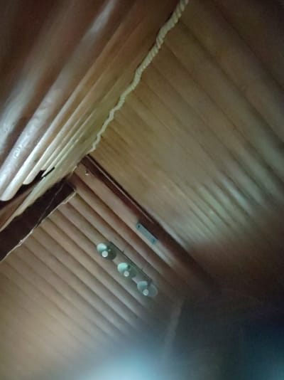 The image is a low-angle, close-up, outdoor shot of a wooden ceiling with a rope running along a seam. There are three small, round lights on the ceiling, and a dark, blurry area in the lower right corner. The image is located in the city of Solnechnyi, Russia.